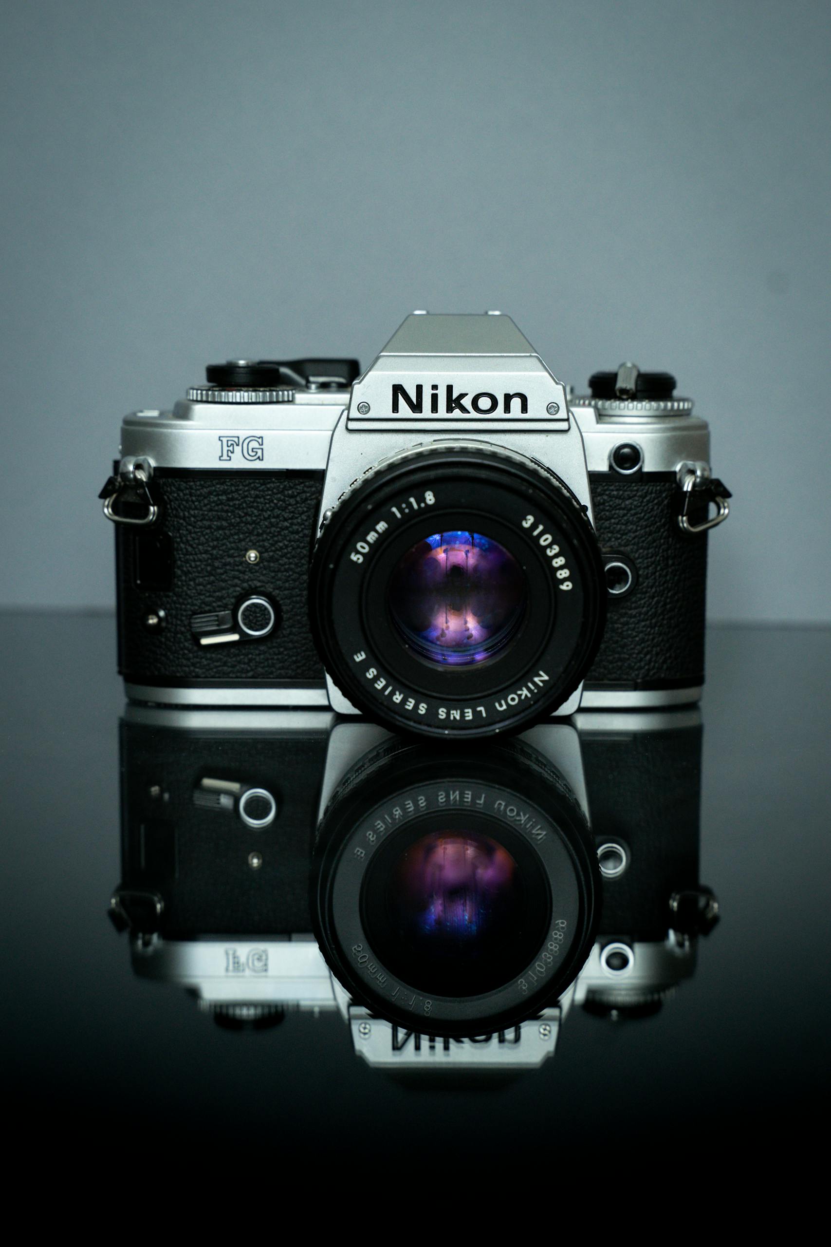 Classic Nikon film camera with reflection on black surface, showcasing vintage photography equipment.