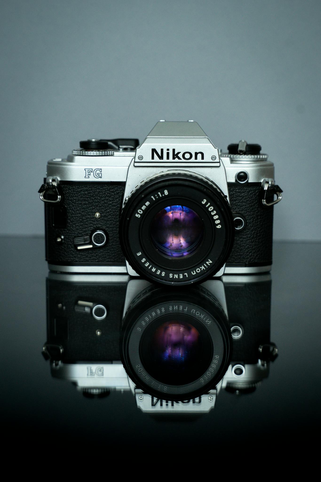 Classic Nikon film camera with reflection on black surface, showcasing vintage photography equipment.